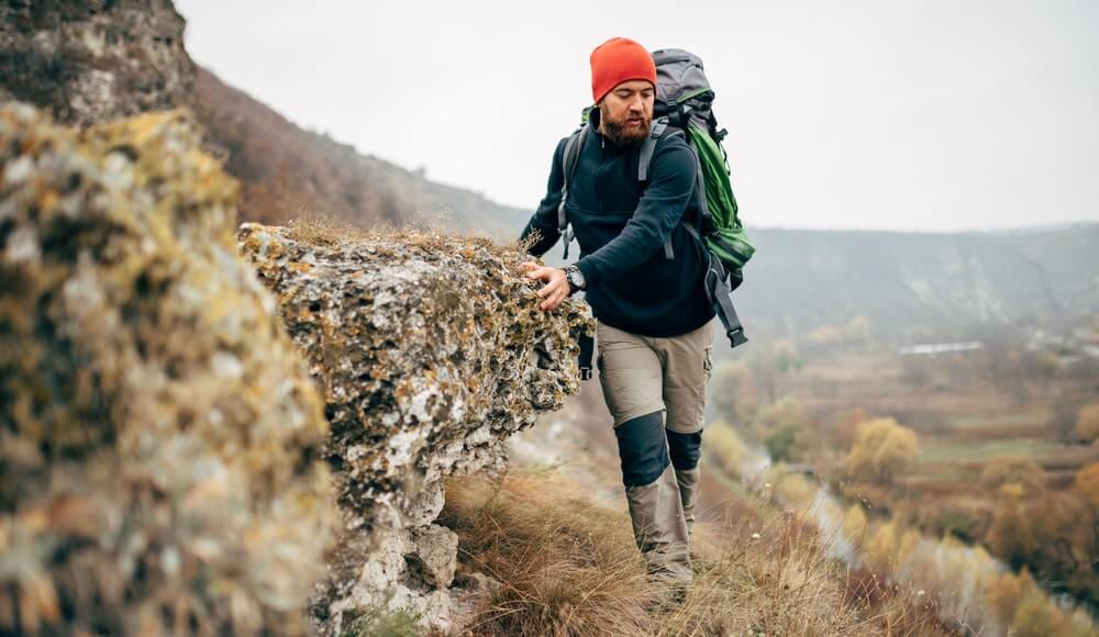Bearded young male hiking in mountains with trave